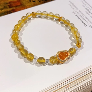 Macro detail of citrine beaded bracelet with a gold gourd pendant on an open book