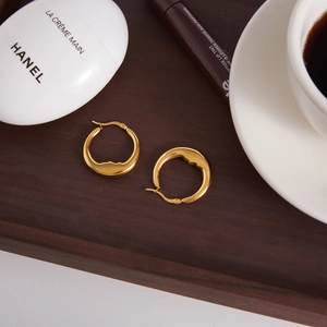 Gold moon-shaped hoop earrings with artistic face profile on a wooden tray
