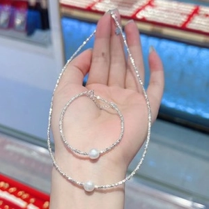 Close-up of sparkling silver chain jewelry set with white pearls held by a hand