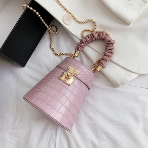 Pink crocodile pattern bucket bag with gold chain strap and pleated handle on white cloth