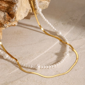 Layered gold flat snake chain and white pearl necklace on natural textured stone