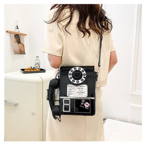 Detail of creative vintage telephone crossbody bag in black patent leather worn by model