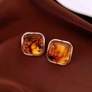 Detailed close-up of square amber earrings on dark brown satin silk fabric background