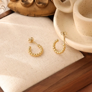 Detailed view of 18K gold plated C-shaped bead earrings on a wooden jewelry tray