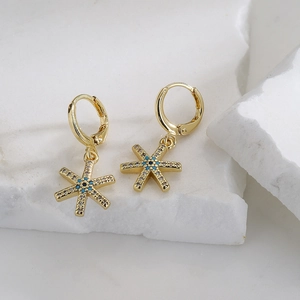 Close-up of 18K gold star earrings with turquoise centers and zircon on white stone
