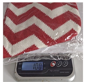 Close-up of a red and white knitted Christmas gift bag on a digital scale weighing 100g