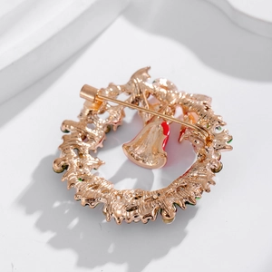 Golden Christmas wreath brooch with bells and rhinestones on white marble background