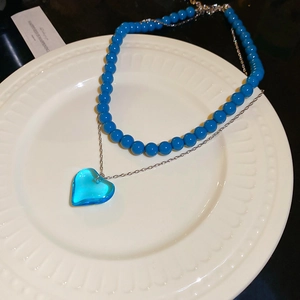 Detail of double-layer necklace with blue beads and transparent heart pendant in white dish