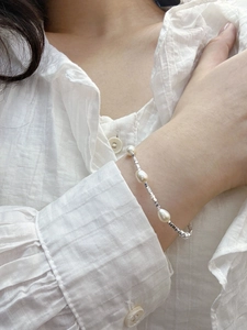 Detail of s925 silver and freshwater pearl bracelet worn on a white striped shirt sleeve