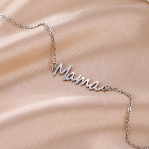 Macro shot of silver Mama pendant on a delicate chain against champagne satin fabric