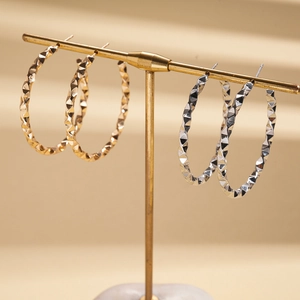 Geometric twisted C-shaped earrings in gold and silver finish on a jewelry display stand