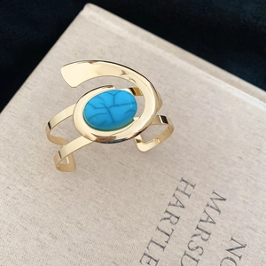 Detail view of a gold-toned open cuff bracelet featuring an oval blue turquoise stone inlay