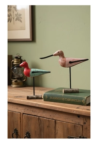 Hand-painted Nordic style wooden bird ornaments with metal stands on a vintage cabinet