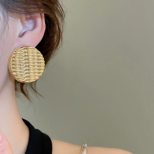 Close-up of golden geometric ripple acrylic stud earrings worn on model ear