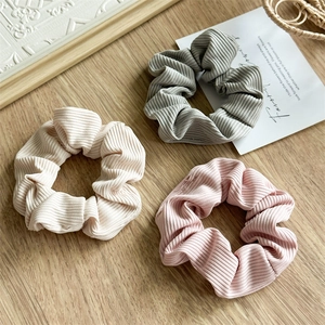 Close-up of three ribbed scrunchies in cream, sage green, and soft pink on wooden table
