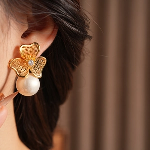 Close-up of a gold clover pearl earring with a zircon stone worn by a female model