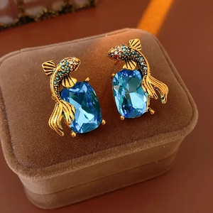 Detail of goldfish earrings with blue gems and crystals on a brown velvet jewelry box