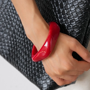 Polished bright red wavy acrylic bangle bracelet shown on model with black leather background