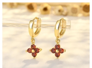 Makro-Detail von goldenen Creolen mit eleganten roten Anhängern in Form von Zirkon-Blüten