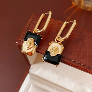 Detail view of gold-plated lion head earrings with black square zircons on leather