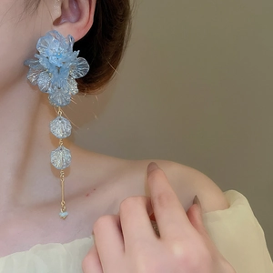 Close-up of elegant blue acrylic flower tassel earrings on model with soft lighting
