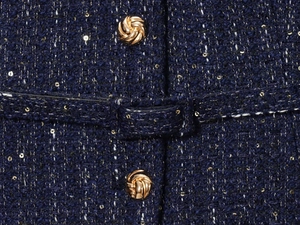 Nahaufnahme von dunkelblauem Tweedstoff mit Pailletten und einem goldenen Metallknopf