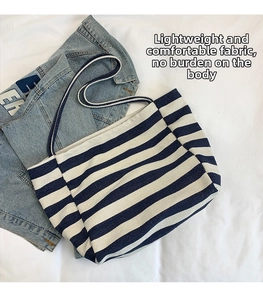 Flat lay of blue and white striped canvas tote bag on a white textured fabric background