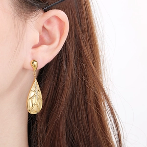 Detail of golden teardrop earring with wing texture and sparkling zircons on ear