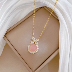 Detail of gold necklace with pink round gemstone pendant and zircon bow on beige cushion