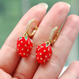 Close-up of strawberry earrings with red enamel and gold details on fingers
