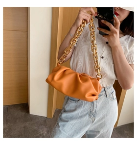 Detail of soft orange leather pleats and chunky gold metal chain on a cloud pouch bag