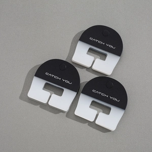 Close-up of matte black and white U-shaped clothing clips with CATCH YOU text
