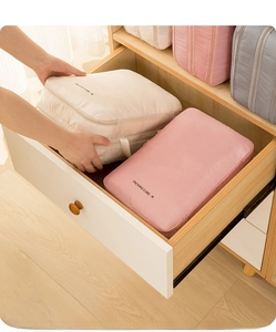 Détail d'une main rangeant des cubes de voyage roses et crème dans un tiroir en bois