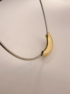 Macro detail of high-polished gold curved tube pendant on a silver snake chain
