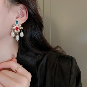 Detail of vintage gold earrings with blue and red stones and pearl tassels worn by a model