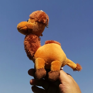 Detail view of a small camel plush toy keychain held against a bright blue sky background