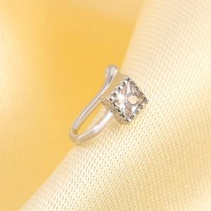 Macro shot of silver non-pierced nose ring with square zircon on yellow silk background