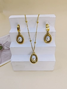 Detail of gold jewelry set with oval pearl pendants on a minimalist white display stand