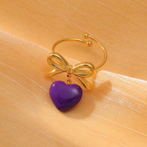 Macro detail of gold bow ring featuring a purple heart pendant on peach fabric