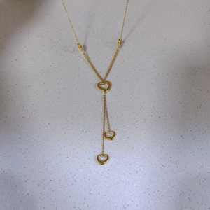 Golden Y-shaped pearl necklace with triple open heart pendants on a stone surface