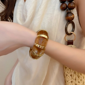 Close-up of amber acrylic link bracelet with gold metal accents worn on a wrist