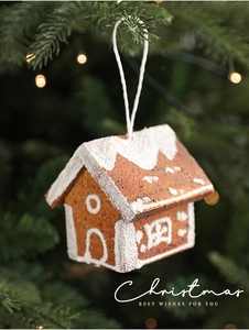 Close-up of gingerbread house Christmas ornament hanging on a pine tree with warm lights