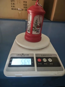 Detail view of a red Christmas mailbox lantern weighing 56.4 grams on a white scale.