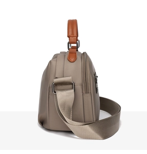 Side view of taupe waterproof oxford bag showing multi-layered zippers and leather handles