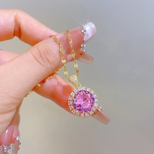 Detail of hand-held gold titanium necklace with a round pink gemstone and pavé diamonds