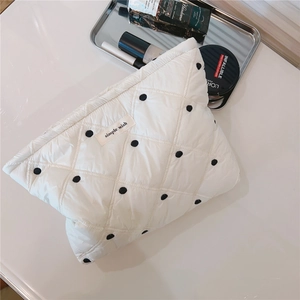 Close-up of white quilted cosmetic bag with black polka dots on a beige surface