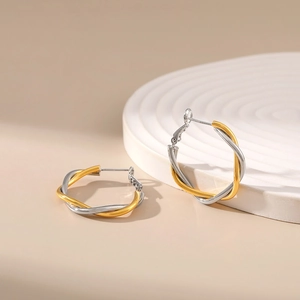 Close-up of gold and silver twisted hoop earrings on a decorative white stand