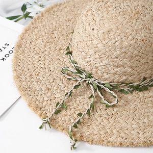 Handcrafted raffia sun hat with green leaf ribbon bow and wide frayed edges for beach