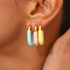 Close-up of three U-shaped earrings in light blue, pink, and yellow on model's ear