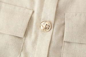 Dettaglio del vestito midi in lino beige con bottoni dorati goffrati e tasca simmetrica